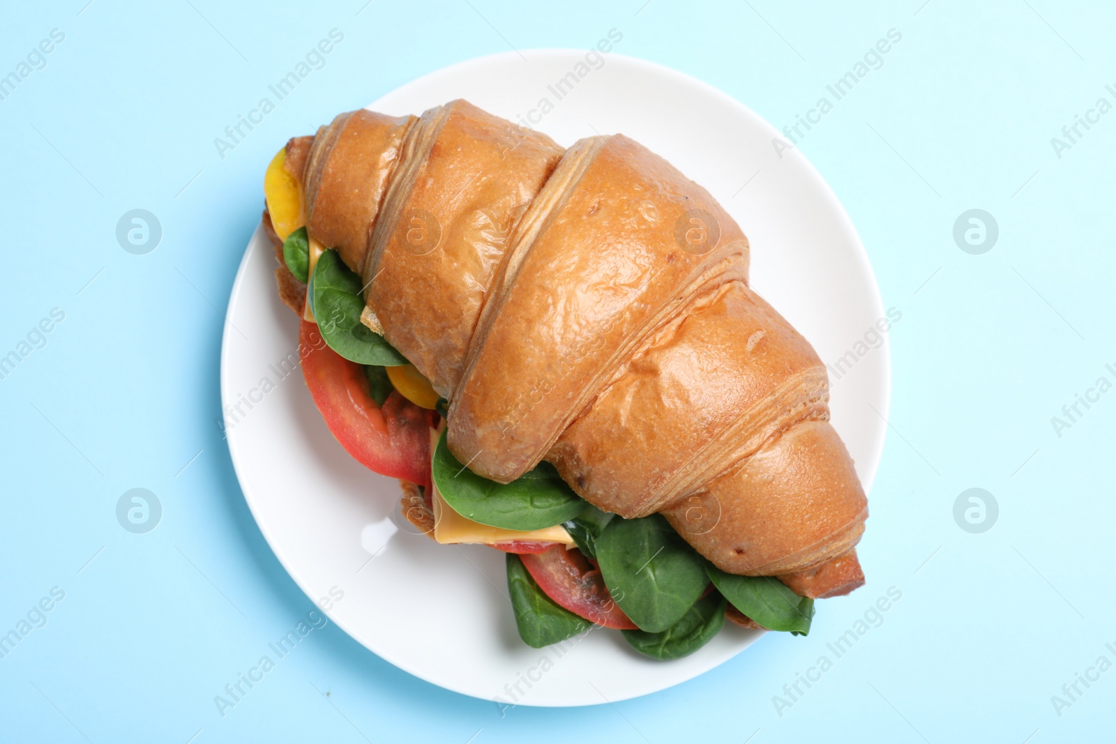 Photo of Tasty vegetarian croissant sandwich on light blue background, top view