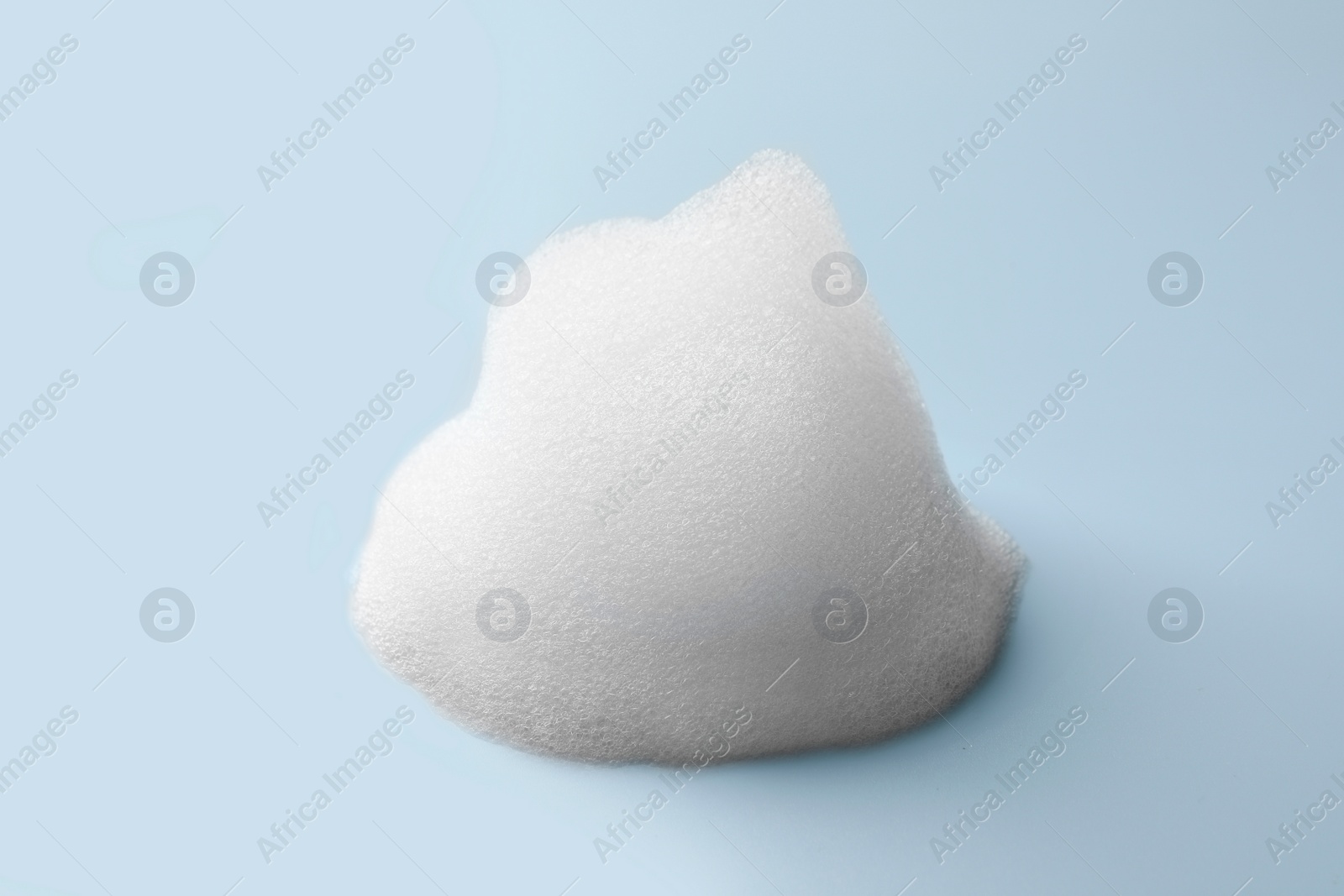 Photo of Drop of fluffy soap foam on light blue background