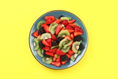 Plate of yummy fruit salad on yellow background, top view