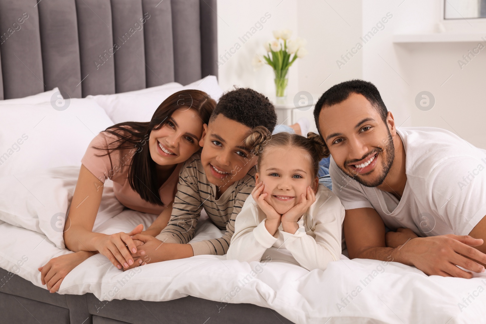 Photo of Happy international family lying on bed at home