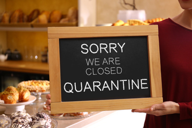 Business owner holding sign with text SORRY WE ARE CLOSED QUARANTINE in bakery, closeup