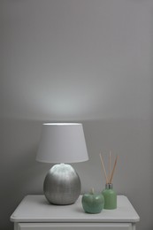 Wooden nightstand with decor and modern lamp near light grey wall. Interior element