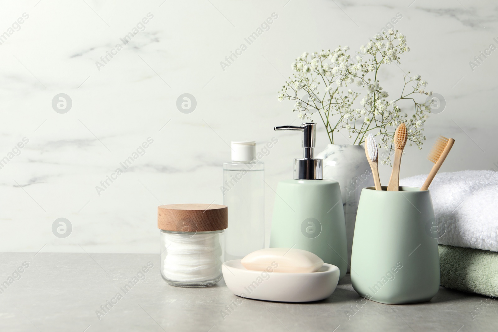 Photo of Different bath accessories, personal care products and gypsophila flowers in vase on gray table near white marble wall, space for text