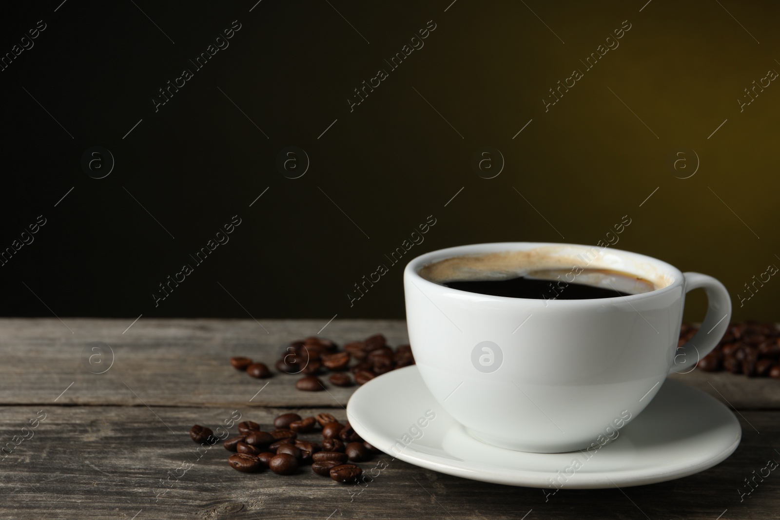 Photo of Cup of hot aromatic coffee and roasted beans on wooden table against dark background, space for text