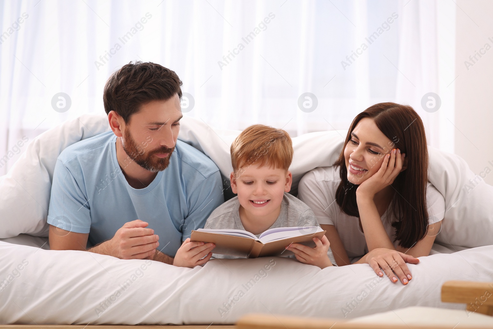 Photo of Happy parents with their child reading book on bed at home