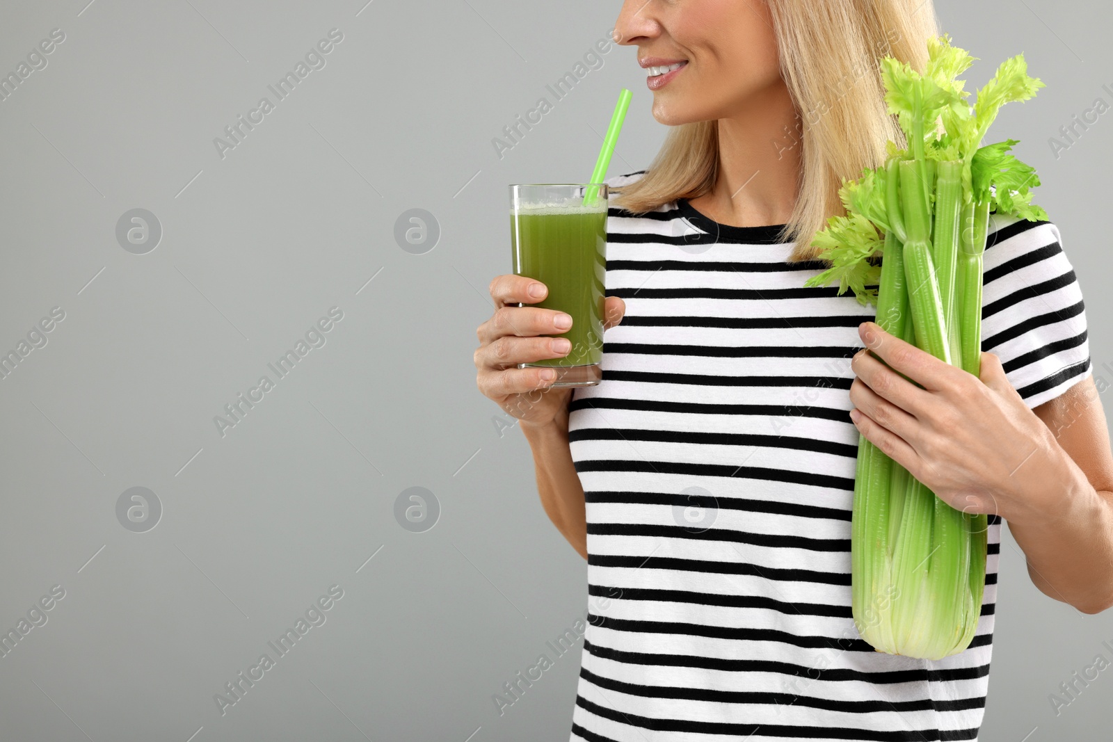 Photo of Woman holding glass with tasty celery juice and fresh vegetable on light grey background, closeup. Space for text