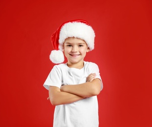 Photo of Cute little child wearing Santa hat on red background. Christmas holiday