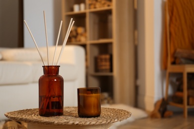 Aromatic reed air freshener and candle on wicker tray in room. Space for text