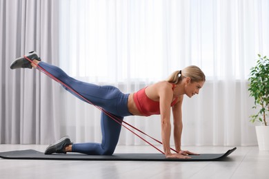 Photo of Athletic woman doing exercise with fitness elastic band on mat at home