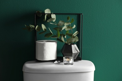 Photo of Decor elements and paper roll on toilet tank near green wall. Bathroom interior