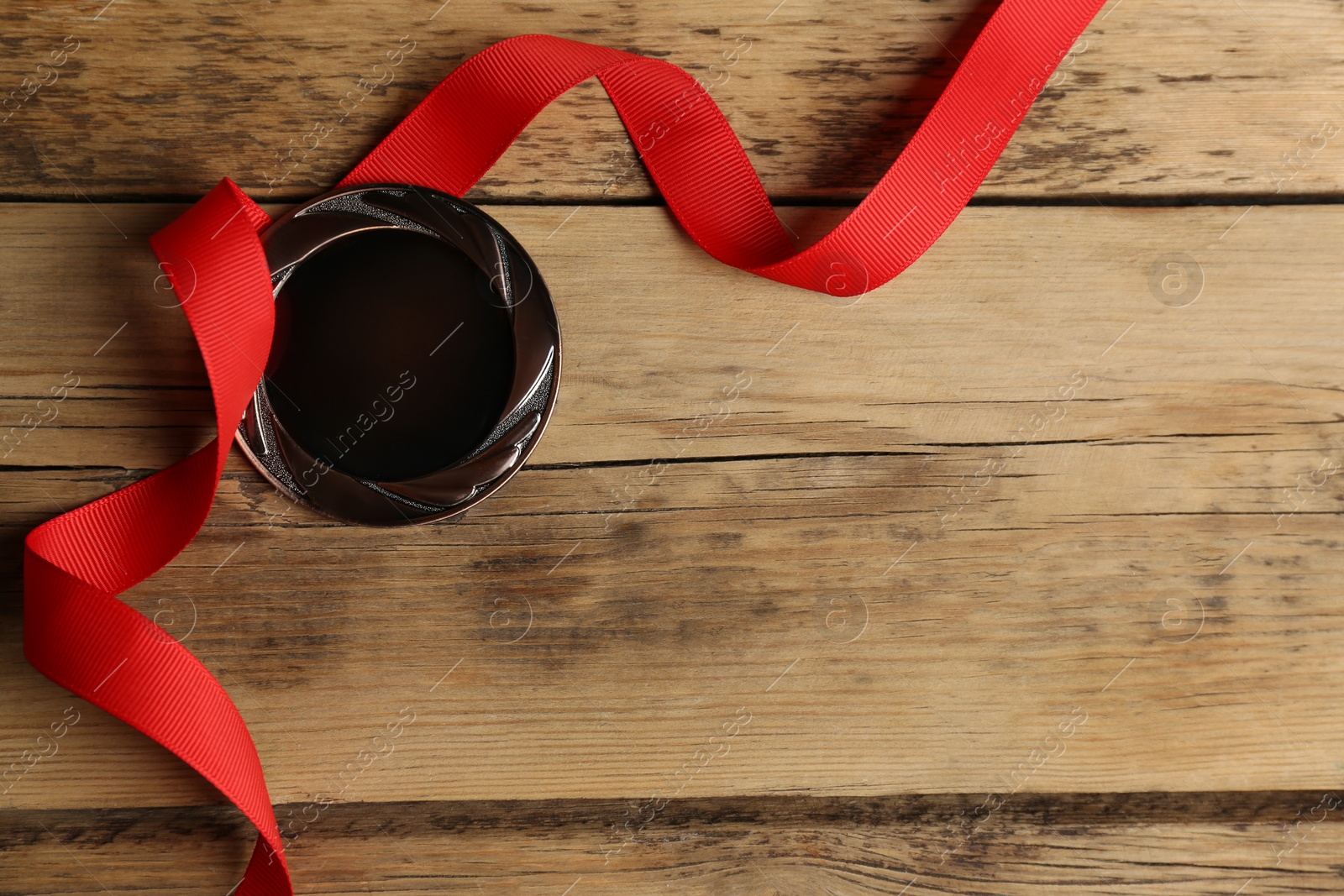 Photo of Bronze medal with red ribbon on wooden background, flat lay. Space for design