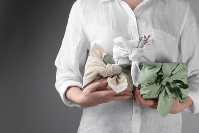 Furoshiki technique. Woman holding gifts packed in different fabrics decorated with plants on gray background, closeup