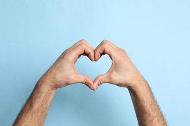 Photo of Man making heart with hands on light blue background, closeup