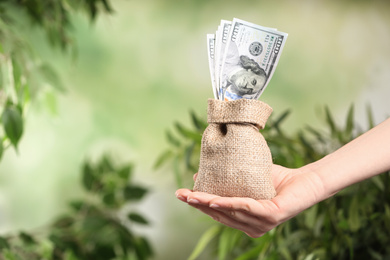 Photo of Woman holding sack with dollars on blurred background, closeup. Money savings