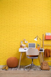 Photo of Stylish home office interior with comfortable workplace near yellow brick wall. Space for text