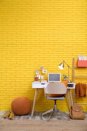 Stylish home office interior with comfortable workplace near yellow brick wall. Space for text