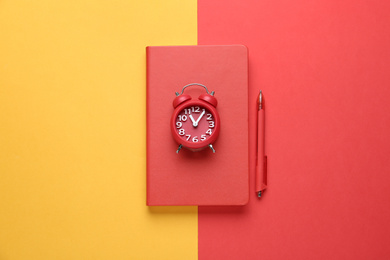 Photo of Red notebook, alarm clock and pen on color background, top view