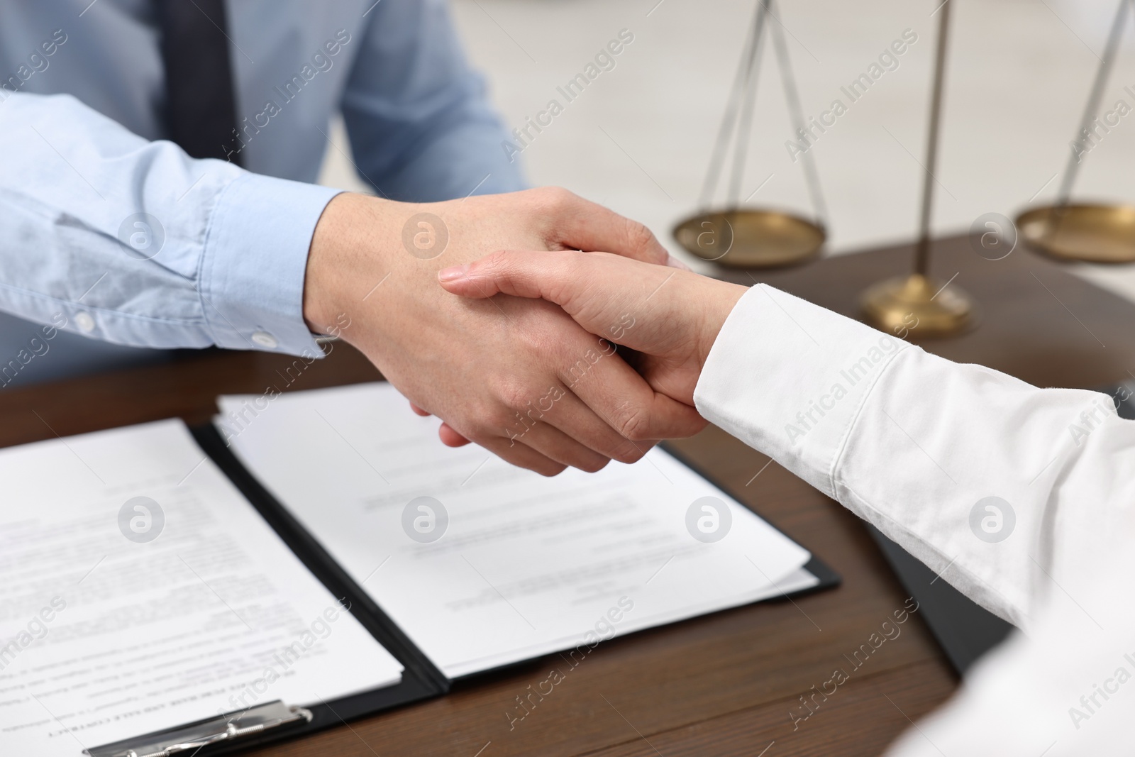 Photo of Lawyers shaking hands at wooden table indoors, closeup