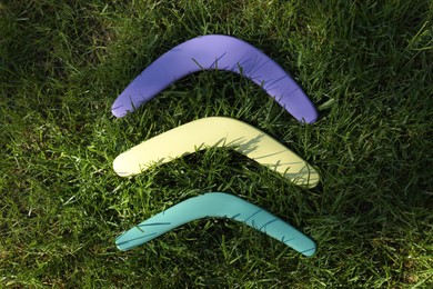 Photo of Violet, yellow and turquoise wooden boomerangs on green grass outdoors, above view