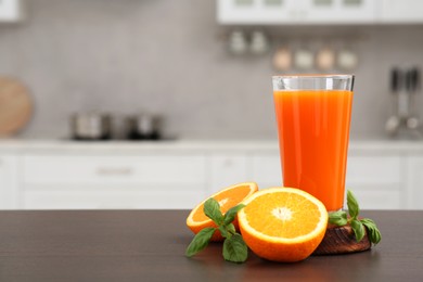 Photo of Glass of tasty orange juice and fruit on wooden counter in kitchen, space for text