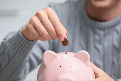 Man putting coin into piggy bank on light background, closeup