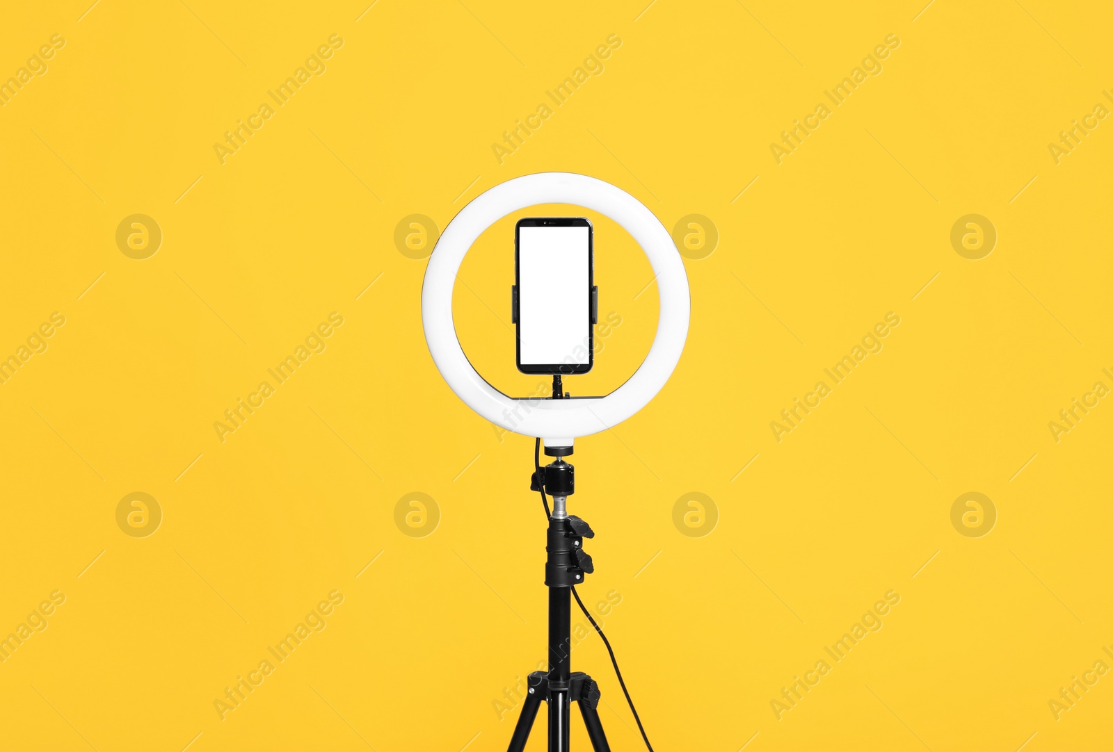 Photo of Modern tripod with ring light and smartphone on yellow background