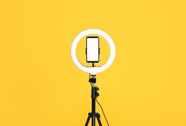 Modern tripod with ring light and smartphone on yellow background