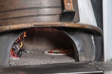 Photo of Burning firewood and tasty pizza in oven at restaurant kitchen