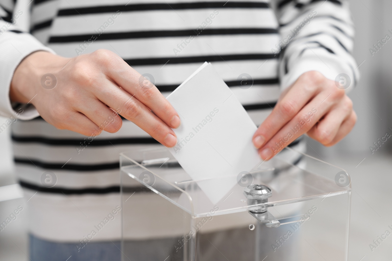 Photo of Woman putting her vote into ballot box on blurred background, closeup