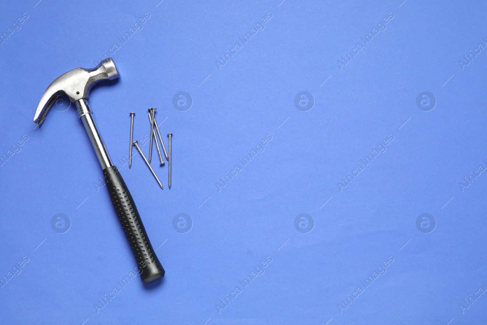 Photo of Hammer and metal nails on blue background, top view. Space for text