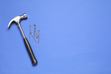 Photo of Hammer and metal nails on blue background, top view. Space for text