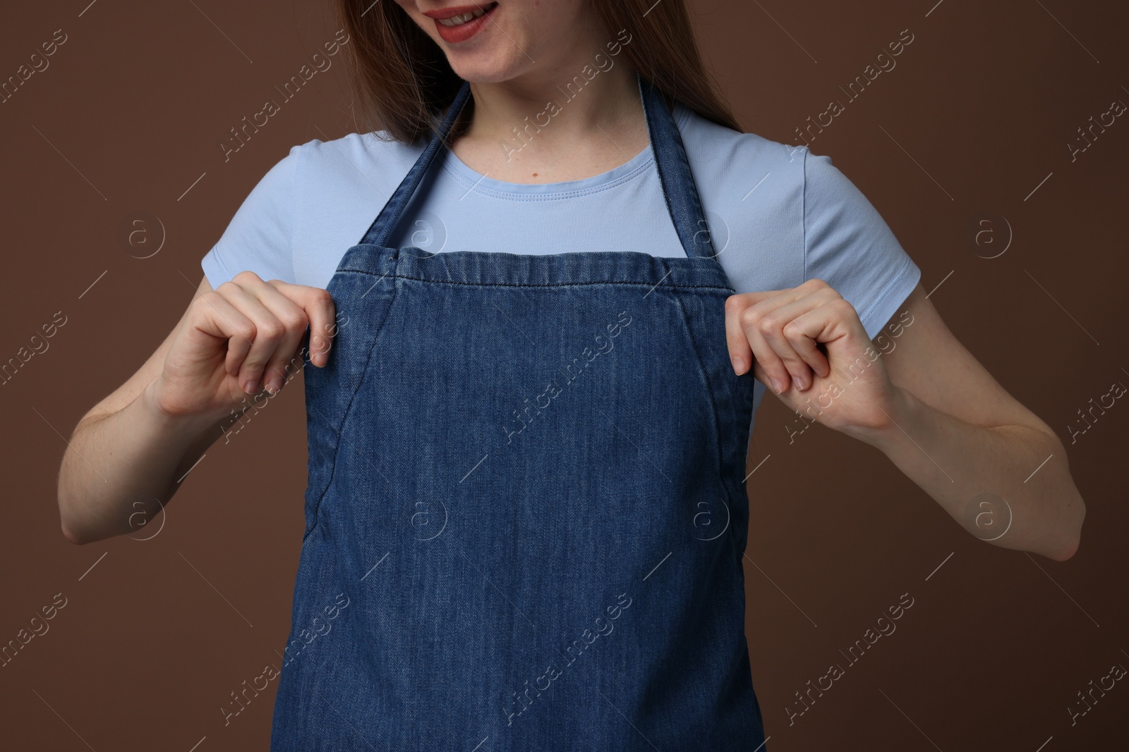 Photo of Woman wearing kitchen apron on brown background, closeup. Mockup for design