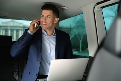 Handsome man with laptop talking on smartphone in modern car