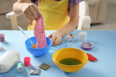 Photo of Little girl making slime toy at table indoors, closeup