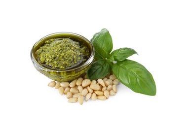 Tasty pesto sauce in glass bowl, pine nuts and basil on white background