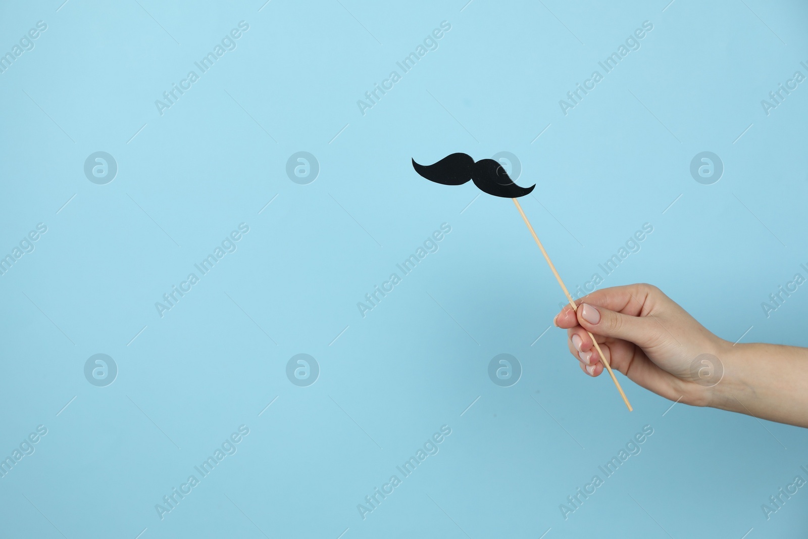 Photo of Woman with fake paper mustache on light blue background, closeup. Space for text