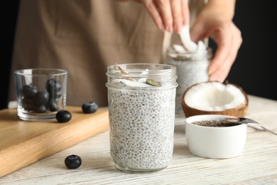 Photo of Jar of tasty chia seed pudding with coconut on table against blurred background
