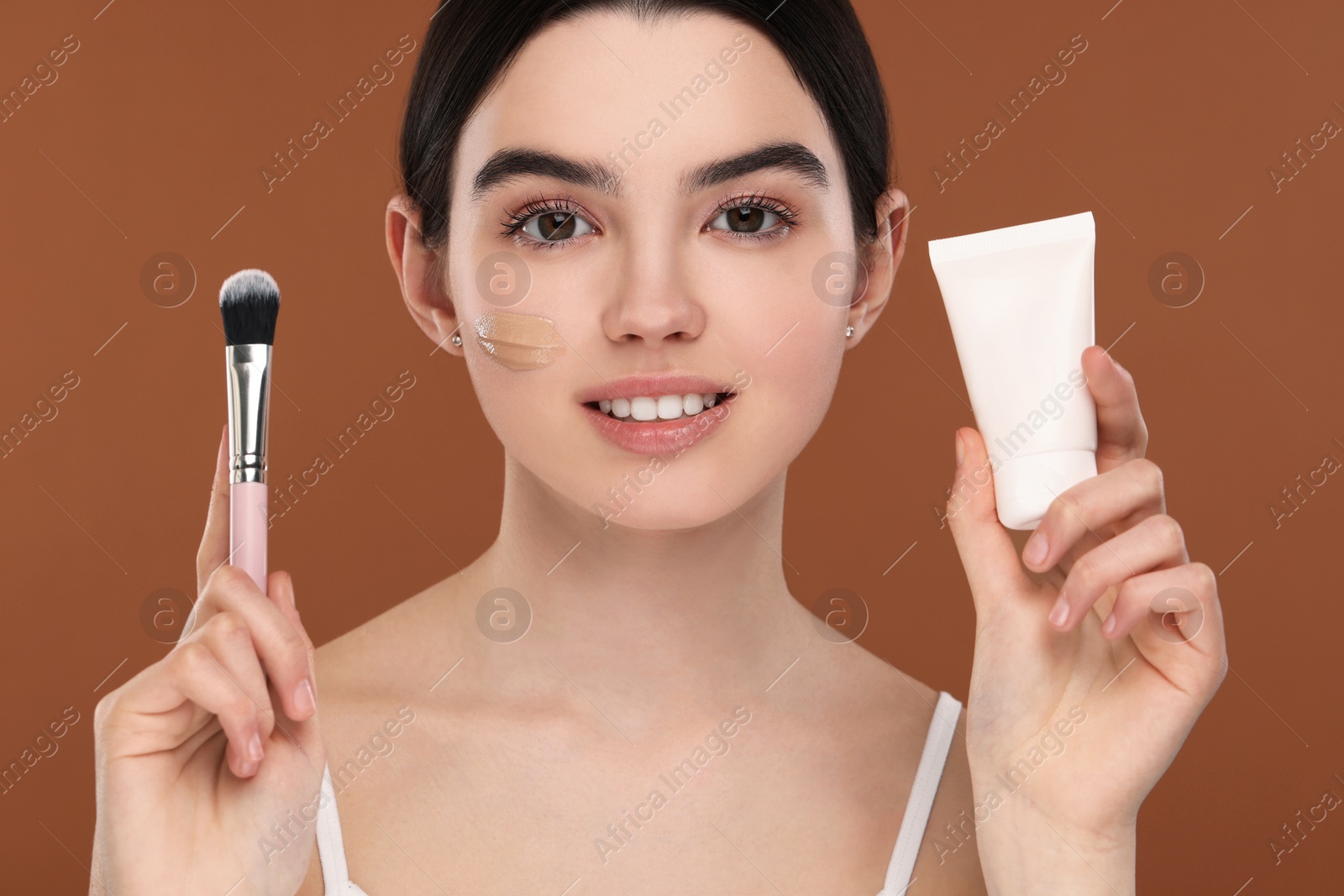 Photo of Teenage girl with tube of foundation and brush on brown background