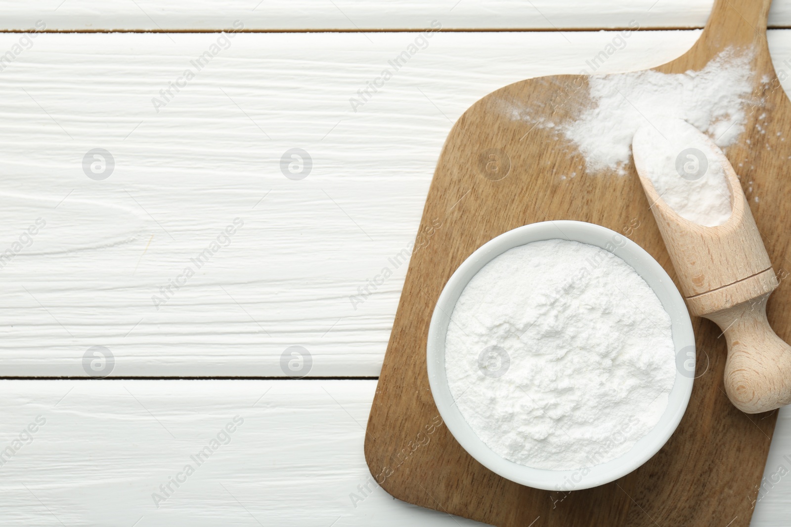 Photo of Baking powder in bowl and scoop on white wooden table, top view. Space for text