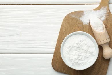 Baking powder in bowl and scoop on white wooden table, top view. Space for text