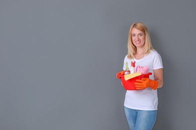 Woman with cleaning supplies on grey background