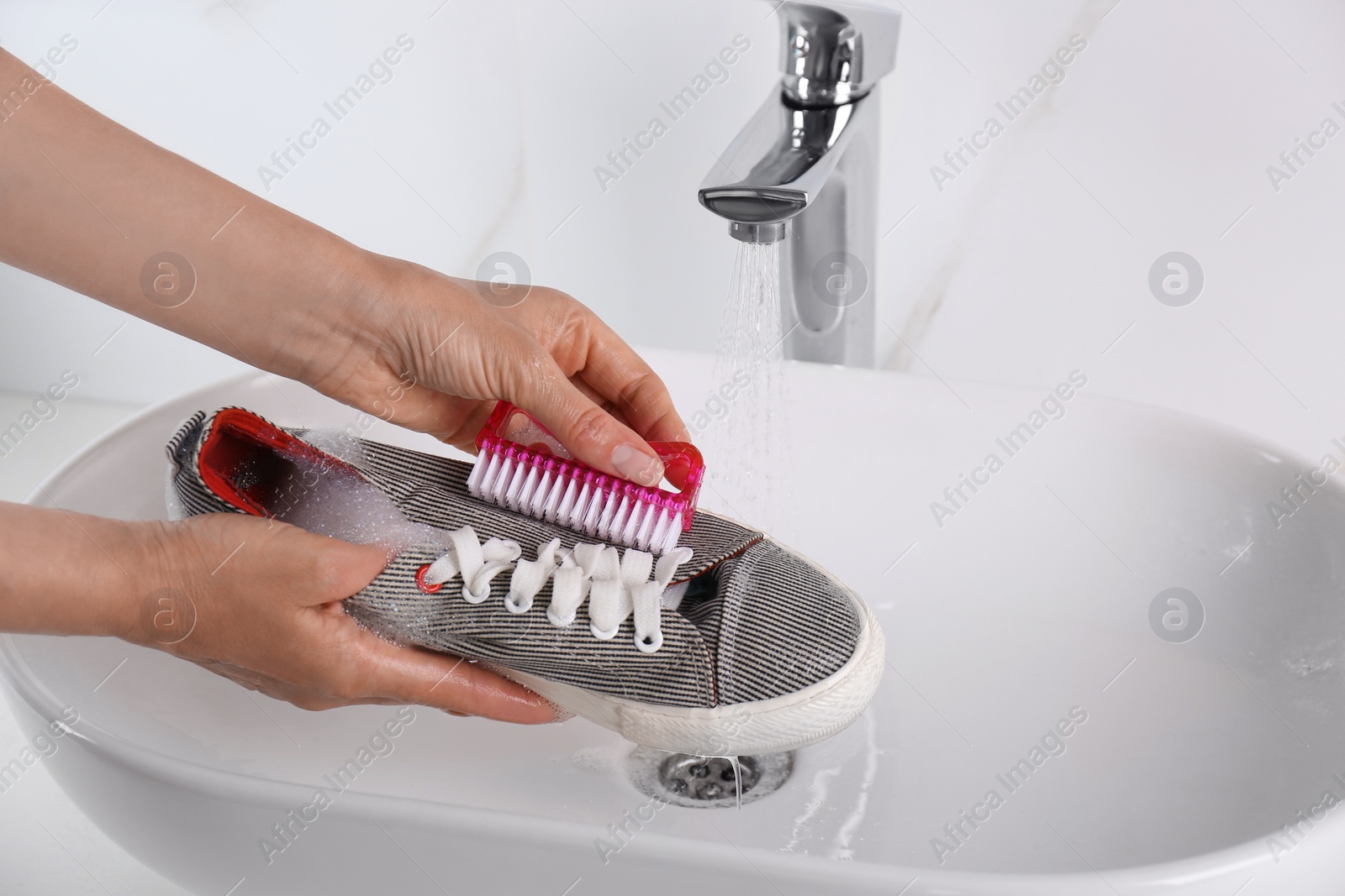 Photo of Woman washing shoe with brush under tap water in sink, closeup