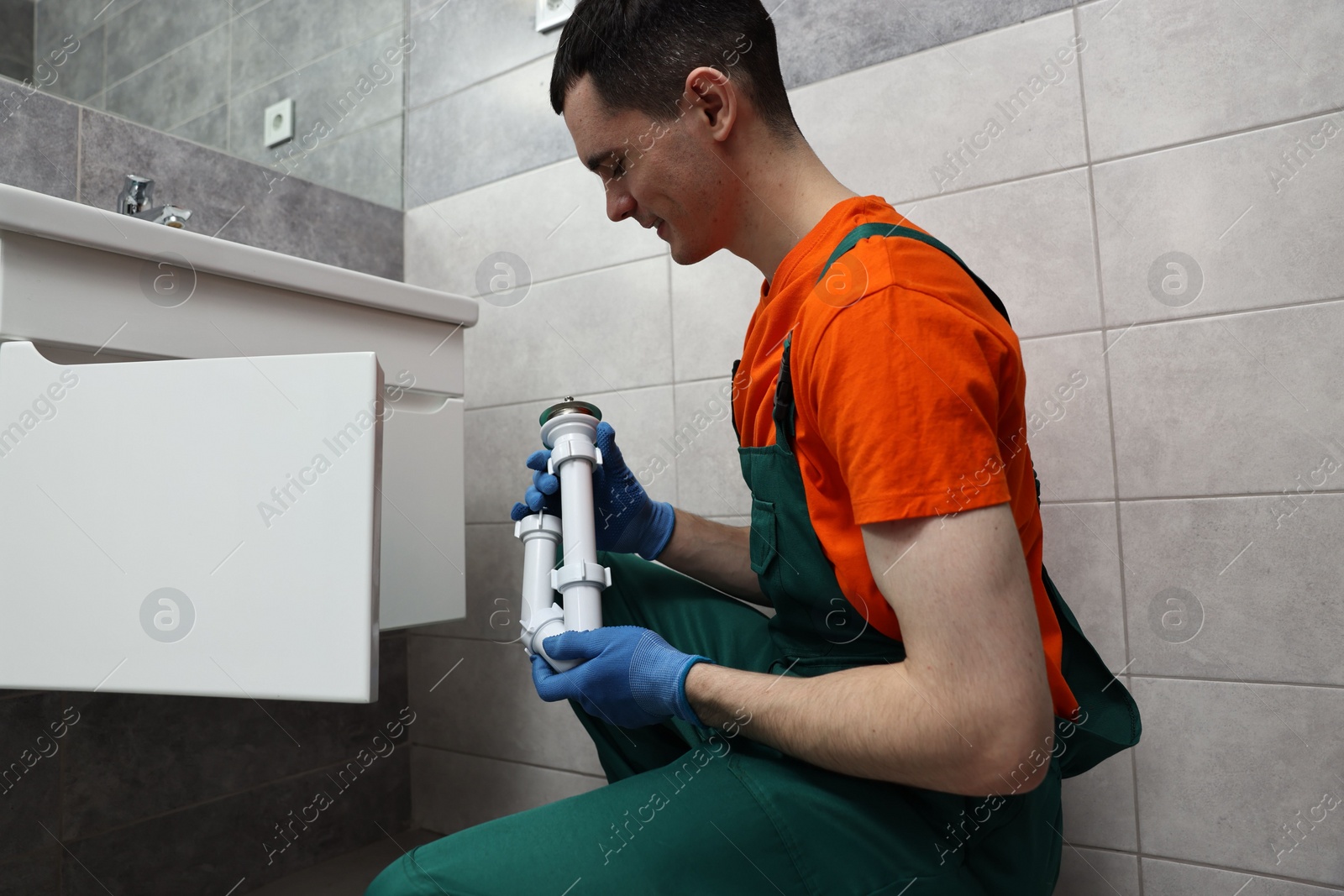 Photo of Young plumber wearing protective gloves repairing sink in bathroom