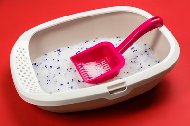 Photo of Cat litter tray with filler and scoop on red background, closeup