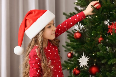 Photo of Little girl decorating Christmas tree at home