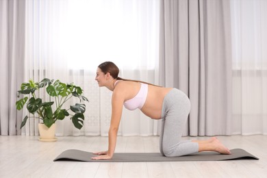 Pregnant woman doing exercises on yoga mat at home