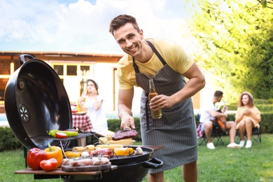 Photo of Young man with beer cooking on barbecue grill outdoors