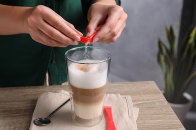 Woman adding sugar to tasty coffee at wooden table, closeup