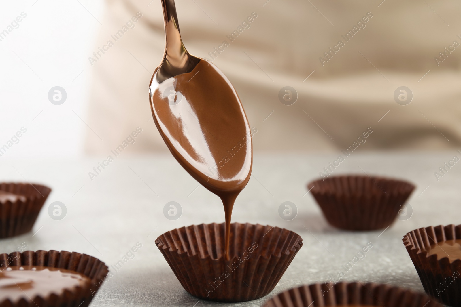 Photo of Professional confectioner making delicious chocolate candies at grey table, closeup