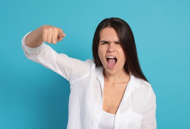 Aggressive young woman pointing on turquoise background
